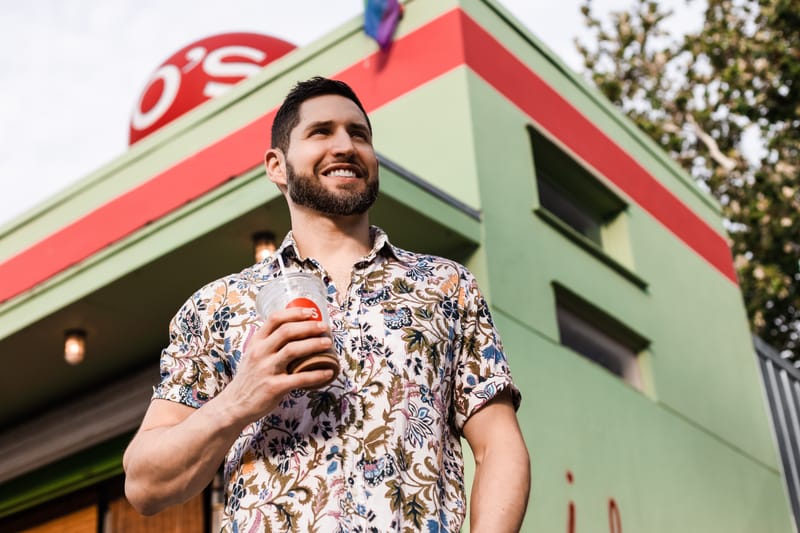David Shapiro holding a drink outside a colorful Austin restaurant, smiling and looking to the side