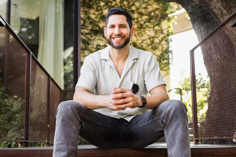 David Shapiro sitting on outdoor steps, smiling, with greenery behind him